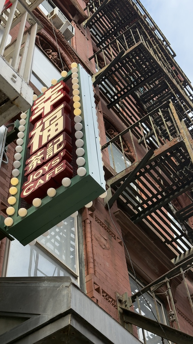 Leuchtschild von Joy's Cafe an einer Backsteinfassade mit Feuertreppen