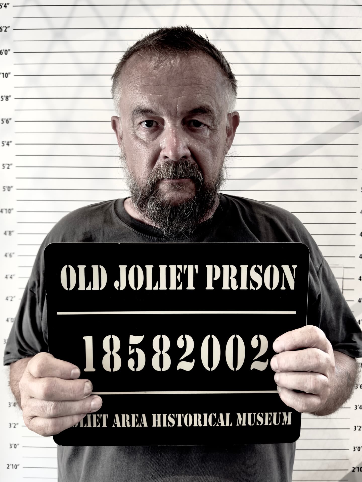 Mugshot-Foto mit Tafel „Old Joliet Prison 18582002“ vor Messwand
