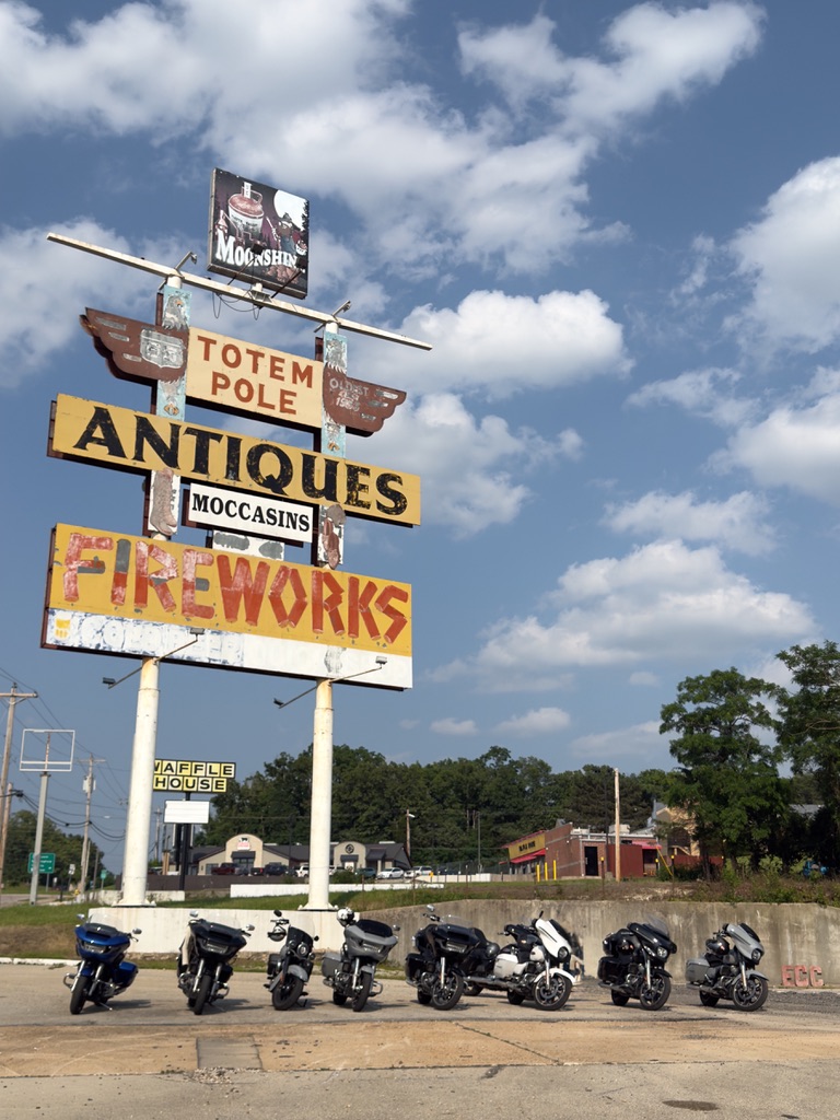 Hohes Blechschild mit Aufschriften Totem Pole Antiques, Moccasins und Fireworks, davor eine Reihe Motorräder