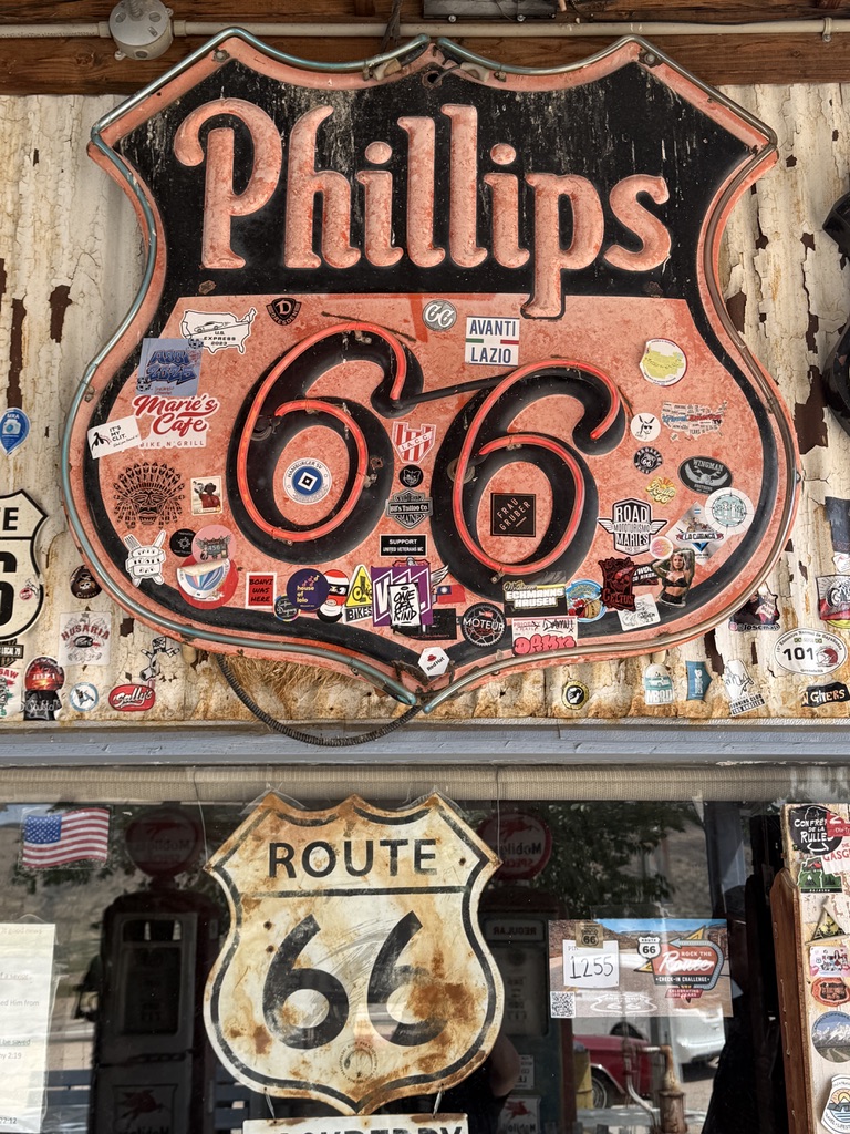 Altes Phillips-66-Blechschild voller Aufkleber über einem verwitterten Route-66-Schild
