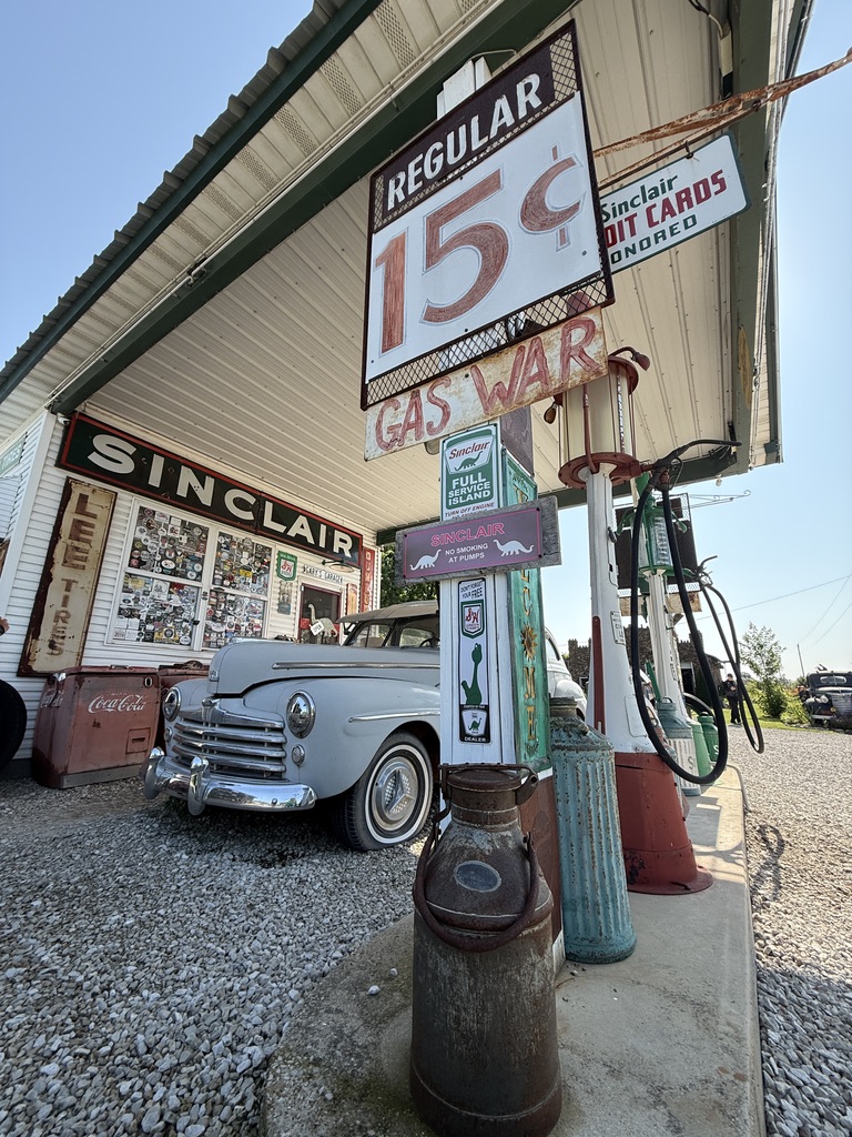 Restaurierte Sinclair-Tankstelle mit Schild „Regular 15 Cents“, Zapfsäulen und Oldtimer