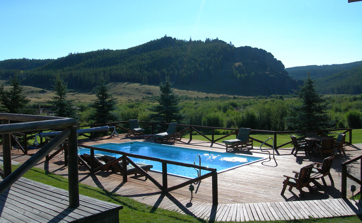 Pool auf der Holzterrasse der Paradise Guest Ranch vor bewaldeten Bergen