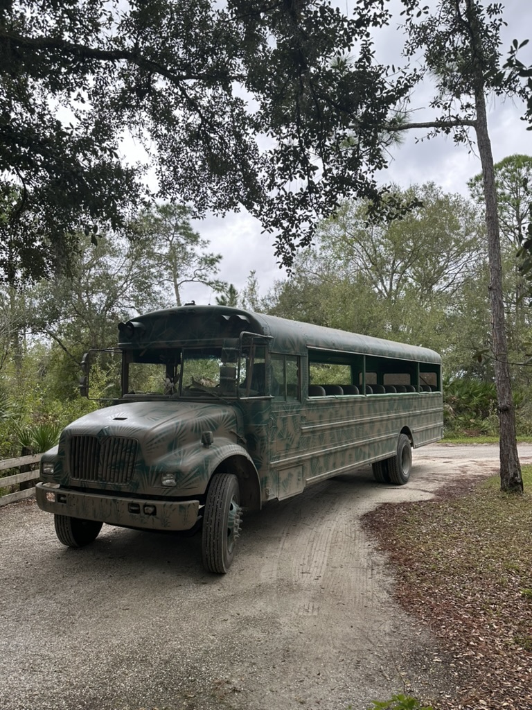 Grün getarnter Safari-Bus auf einem Sandweg unter Bäumen