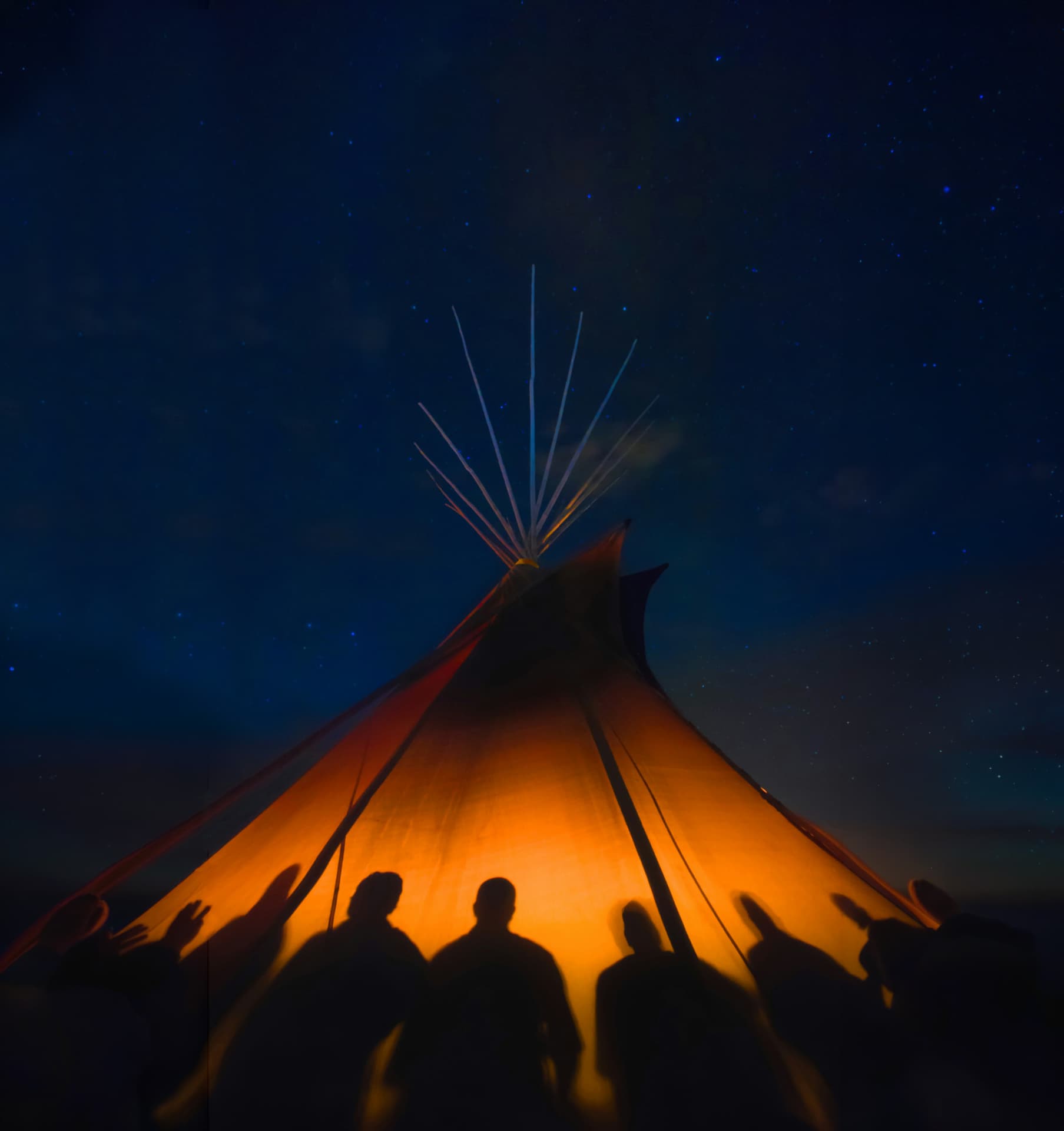 Beleuchtetes Tipi mit Silhouetten unter dem Sternenhimmel
