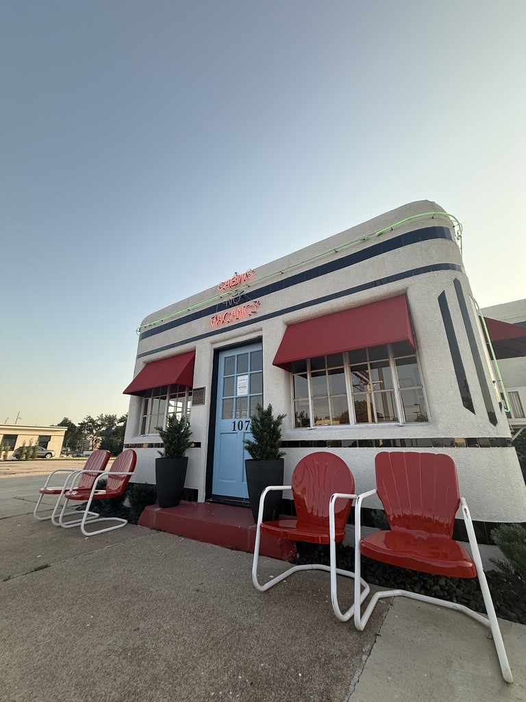 Boots Court Motel mit Neonschrift „Cabins No Vacancy“, roten Metallstühlen und blauer Zimmertür 107