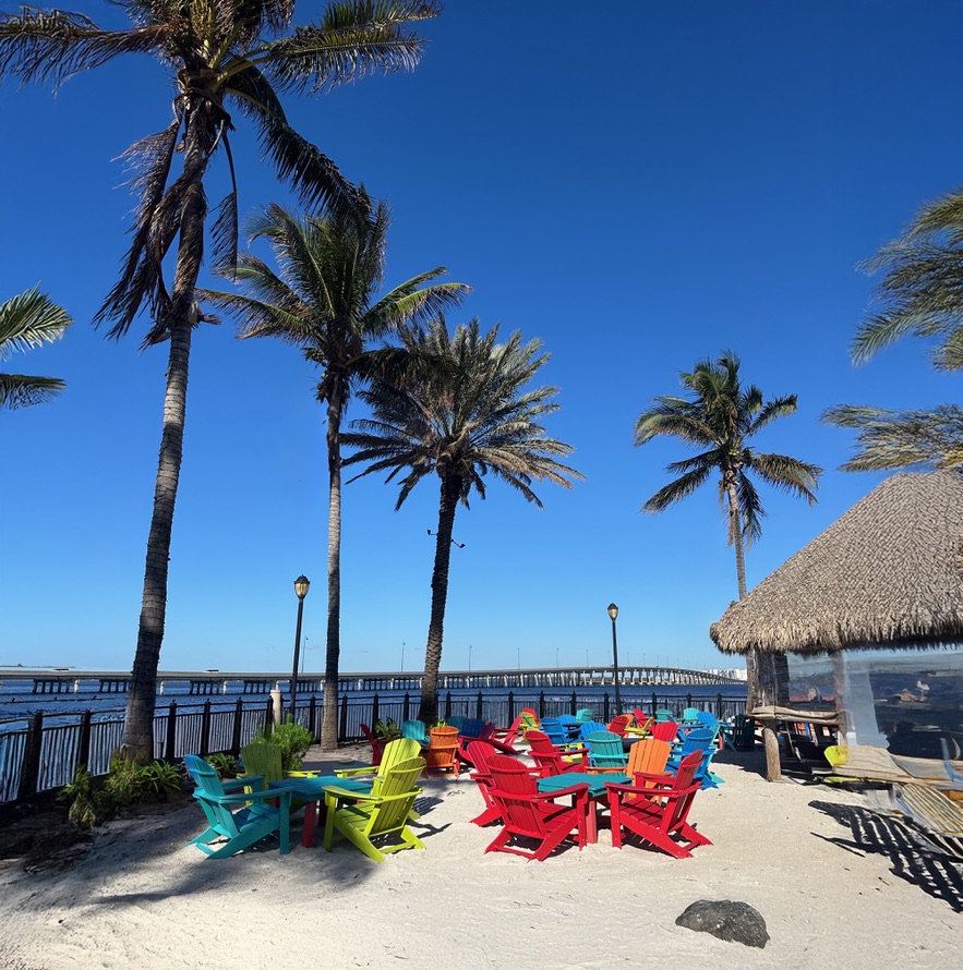 Bunte Stühle im Sand unter Palmen an einer Beachbar in Punta Gorda, Florida
