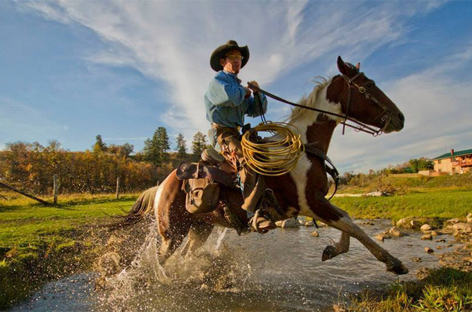 Cowboy galoppiert mit Lasso durch einen Bach