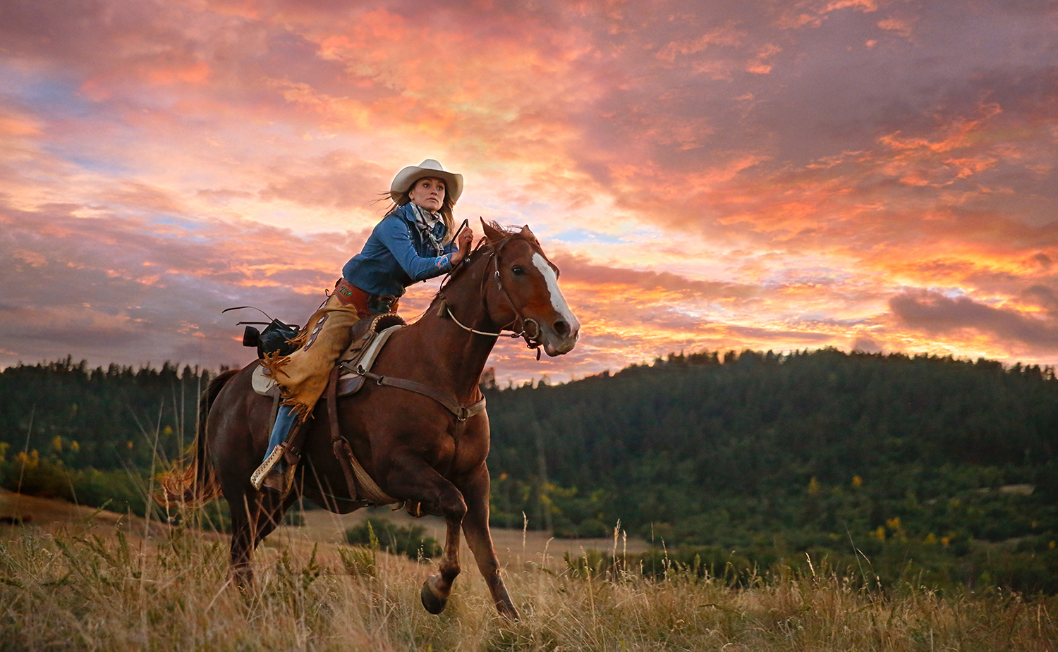 Reiterin im Galopp über eine Wiese der Diamond 7 Bar Guest Ranch bei Sonnenuntergang