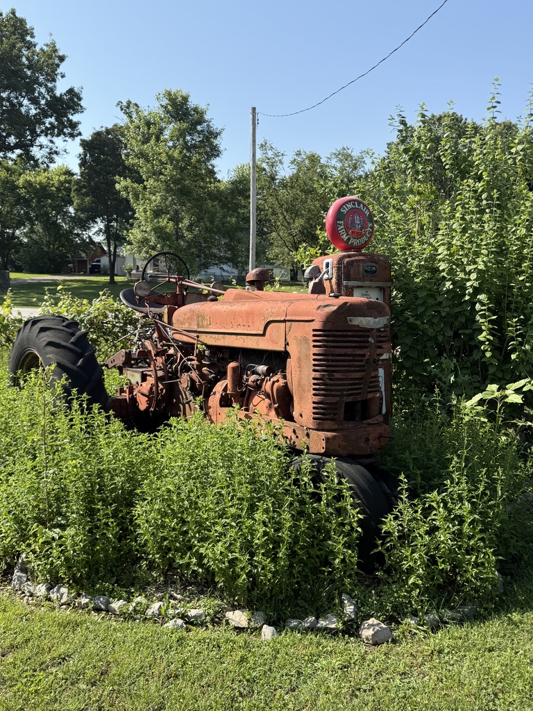 Alter roter Traktor neben einer Sinclair-Zapfsäule im Grünen