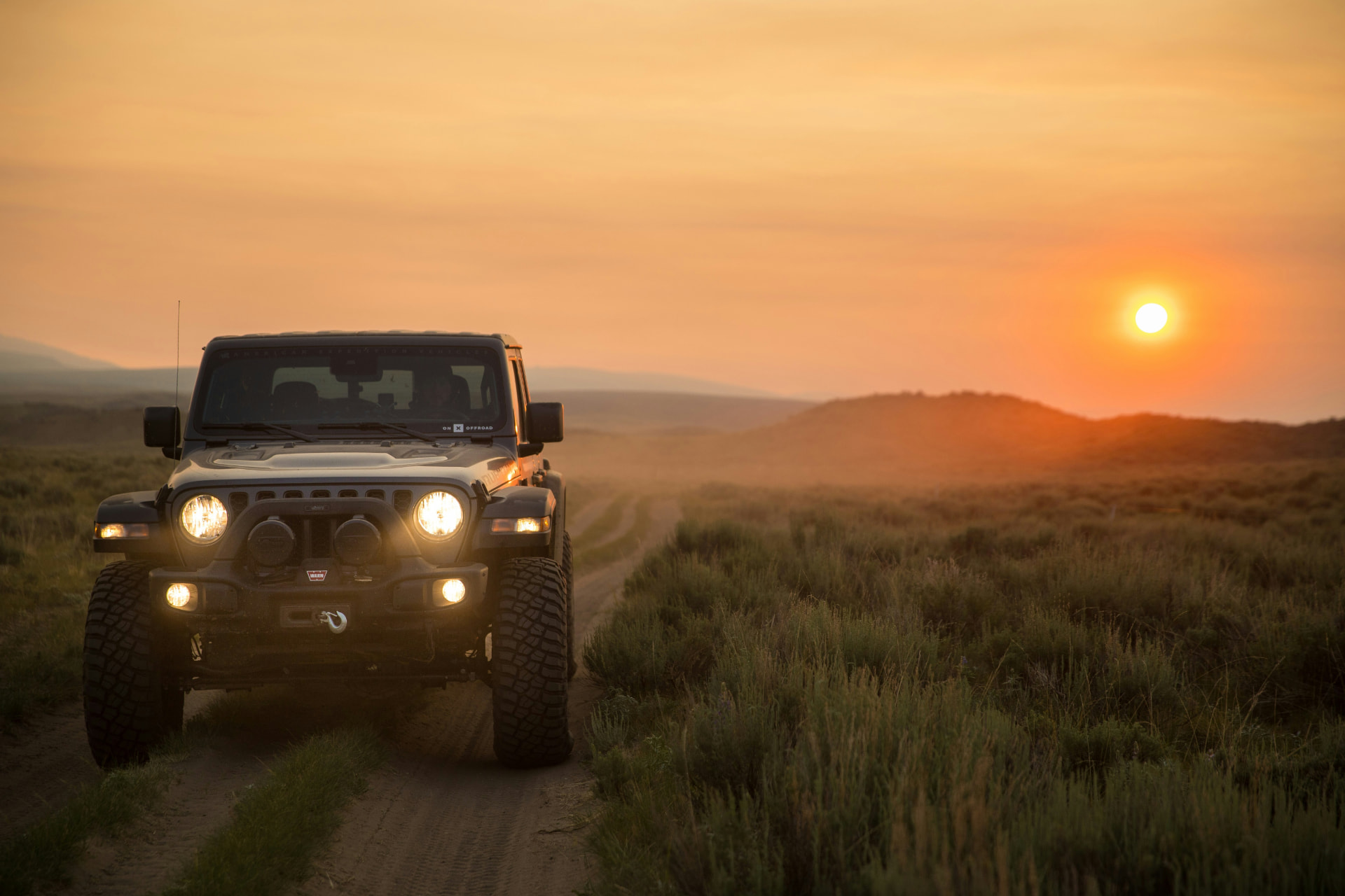 Geländewagen auf einer Schotterpiste in der Prärie bei Sonnenuntergang